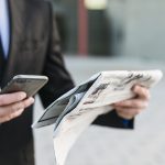 Homem segurando o jornal em papel e o celular